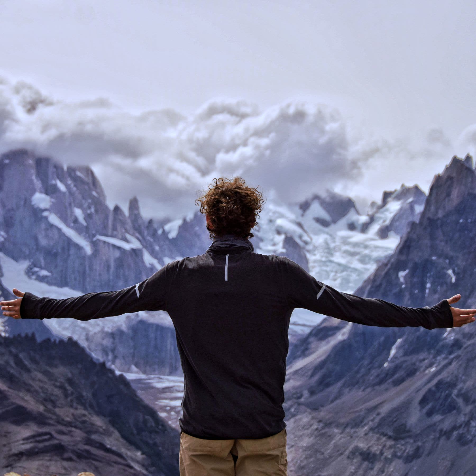 A person standing with open arms in front of a mountain range