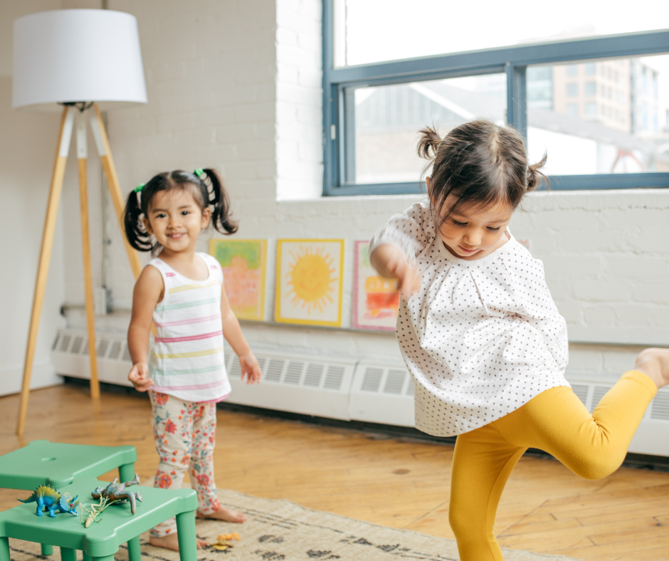 Deux petites filles jouent dans un salon, en premier plan une petite fille en legging rose et des dinosaures.